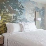 Bed in hotel with white linens and colorful abstract print wallpaper
