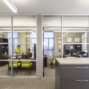 Two people talking in office behind glass walls with large file cabinets in foreground