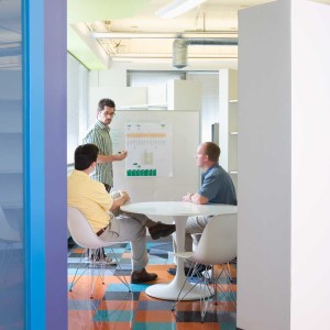 Three men talking at table and whiteboard in colorful office space