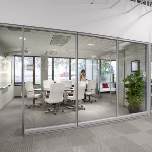 Woman standing in modern conference room seen through glass wall with office next door