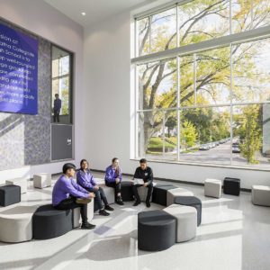 Four students sitting and talking in large two story entrance hall of collegiate high school