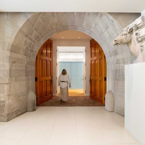 A woman walking through an arched stone entrance to an old carraiage house in a museum in an old mansion