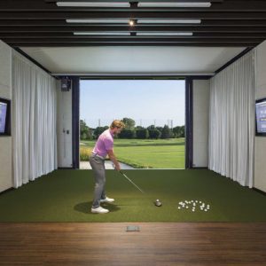 Man hitting a golf ball out large opening in hitting bay at high end golf club