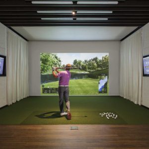 Man hitting a golf ball into simulator screen in hitting bay at high end golf club