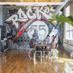 Employees gathered in colorful office lunchroom with grafitti style illustration on wall