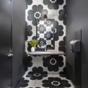 Commercial bathroom with black walls and ceiling and large black and white floral pattern wall and floor tiles