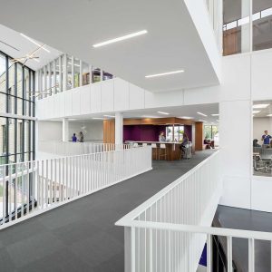 Looking across walkway above interior atrium between two sections of building with view into classrooms and gathering area
